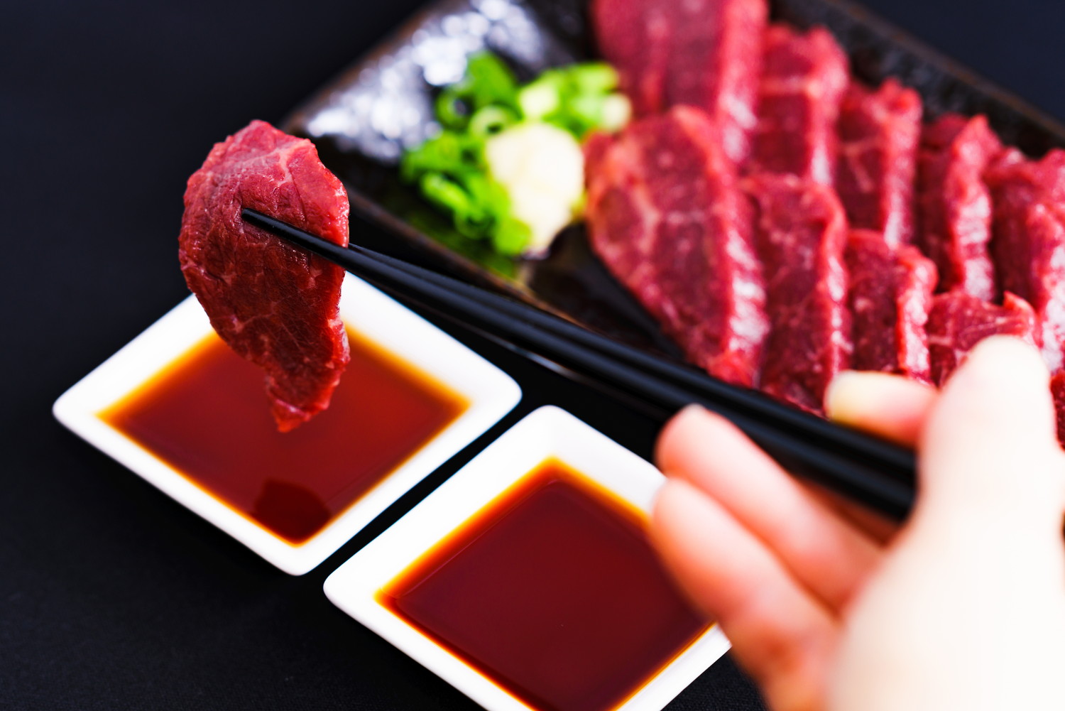 箸で持った馬刺しをたれにつけようとしている人の手